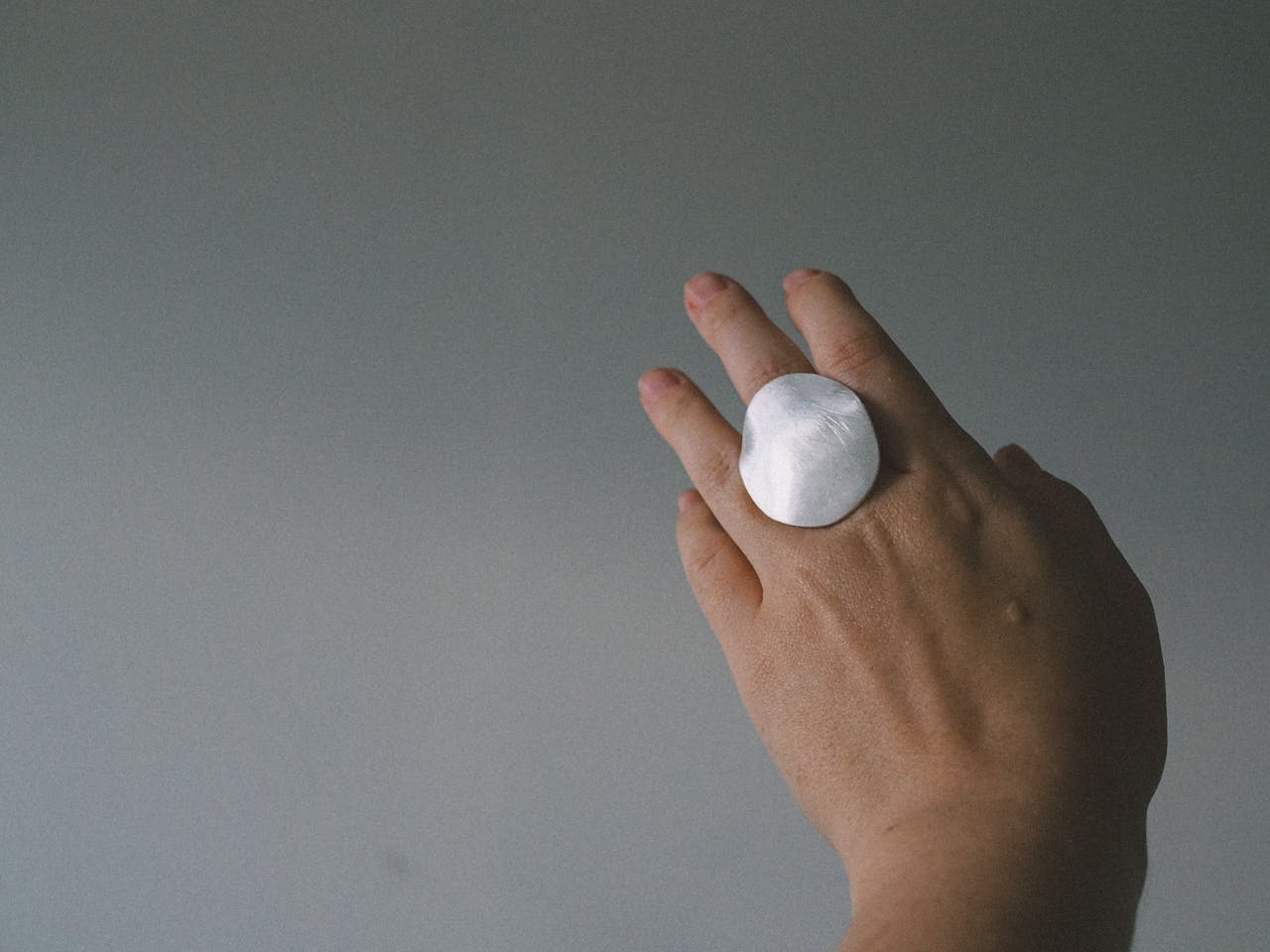 A close-up of a hand wearing a sleek, minimalist silver ring against a neutral background.